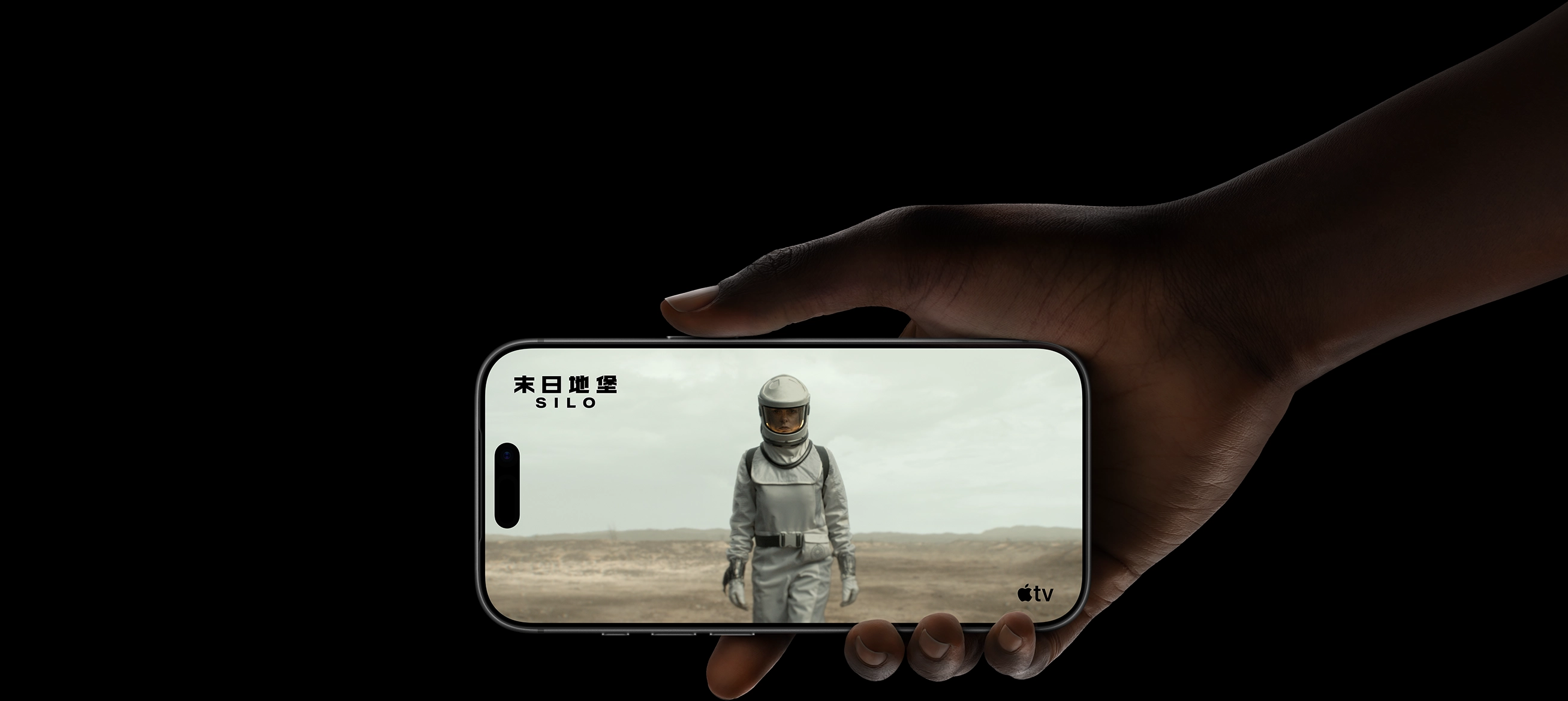 A hand holding iPhone 17 Pro, displaying a woman wearing a protective suit and helmet, walking through a barren landscape. Apple TV logo, series title: Silo
