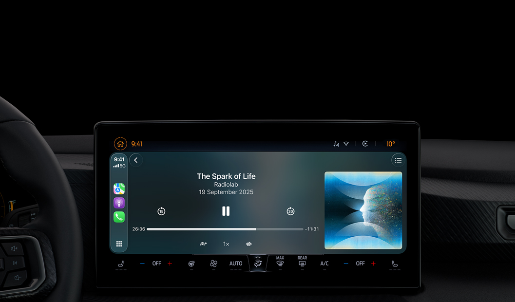 A car interior, centre console display shows Apple Podcasts playing via CarPlay, now playing “The Spark of Life” podcast by Radiolab, playback controls include skip back, pause and skip forward.