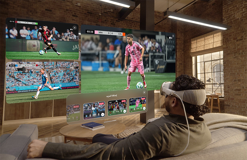 شخص يضع Apple Vision Pro على وجهه ويجلس على أريكة في غرفة الجلوس، وأمامه شاشة كبيرة إلى جانب شاشتين أصغر حجماً، وكل واحدة منها تعرض فعالية رياضية مختلفة. وفي أسفل الشاشة الكبيرة، تظهر نافذة اختيار كُتبت عليها عبارة إضافة المزيد