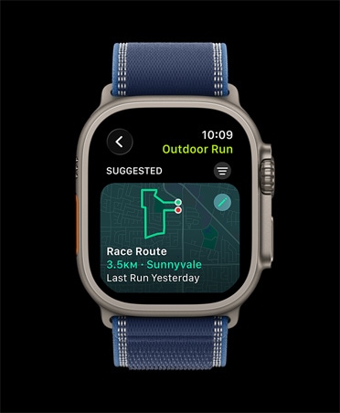 Apple Watch Ultra 3 z kopertą z tytanu w kolorze naturalnym, widać funkcję Wyścig na trasie, trening Bieg w plenerze, zegarek ma opaskę Trail w kolorze niebieskim/jasnoniebieskim