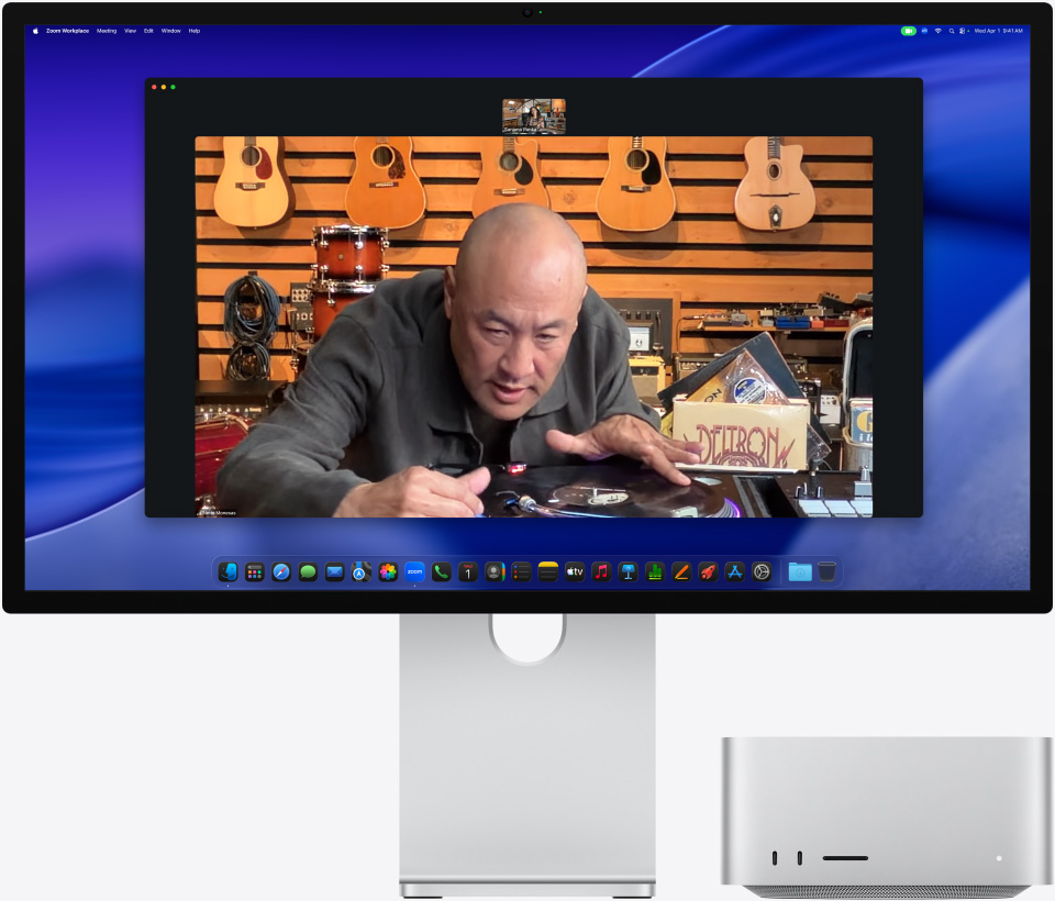 Na displeji Studio Display XDR, pod ktorým je zasunutý Mac Studio, prebieha videohovor, ktorého účastník si v obchode s hudobnými nástrojmi prezerá vystavený gramofón