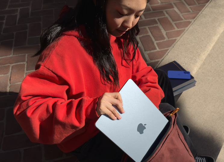 Person som sitter på en stentrappa och lägger MacBook i ryggsäcken.