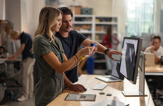 Two students collaborate with a real component model while viewing a 3-D project on a Mac Studio Display, MacBook, Apple Pencil and iPad rest on table
