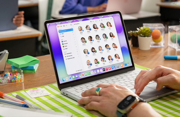 A teacher sits with an open Mac, and the Classroom app shows a full student list on screen