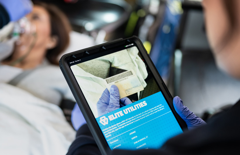 L’app Elite Utilities est ouverte sur un iPad, et un ambulancier paramédical balaie le permis de conduire d’une personne allongée sur une civière
