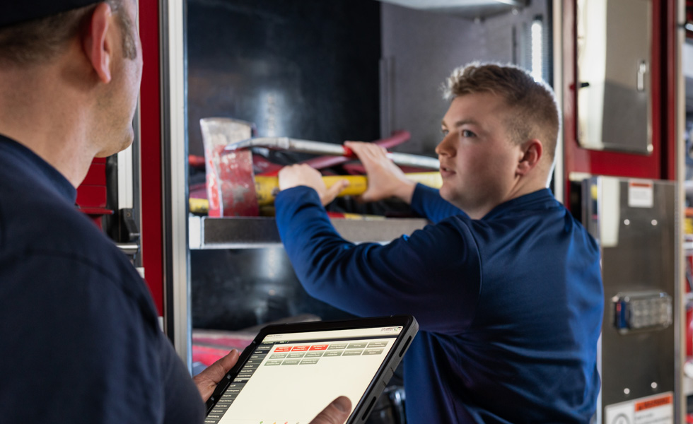 Deux membres de l’équipe inspectant les outils et l’équipement d’un camion d’incendie, l’un d’eux tenant un iPad et l’autre effectuant une inspection