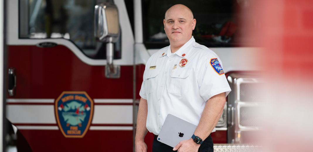 The fire chief stands in front of a fire engine holding an iPad and wearing an Apple Watch