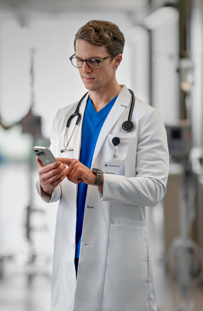 Ein Arzt schaut in einem Krankenhaus auf sein iPhone und überprüft den Fortschritt von Patient:innen.