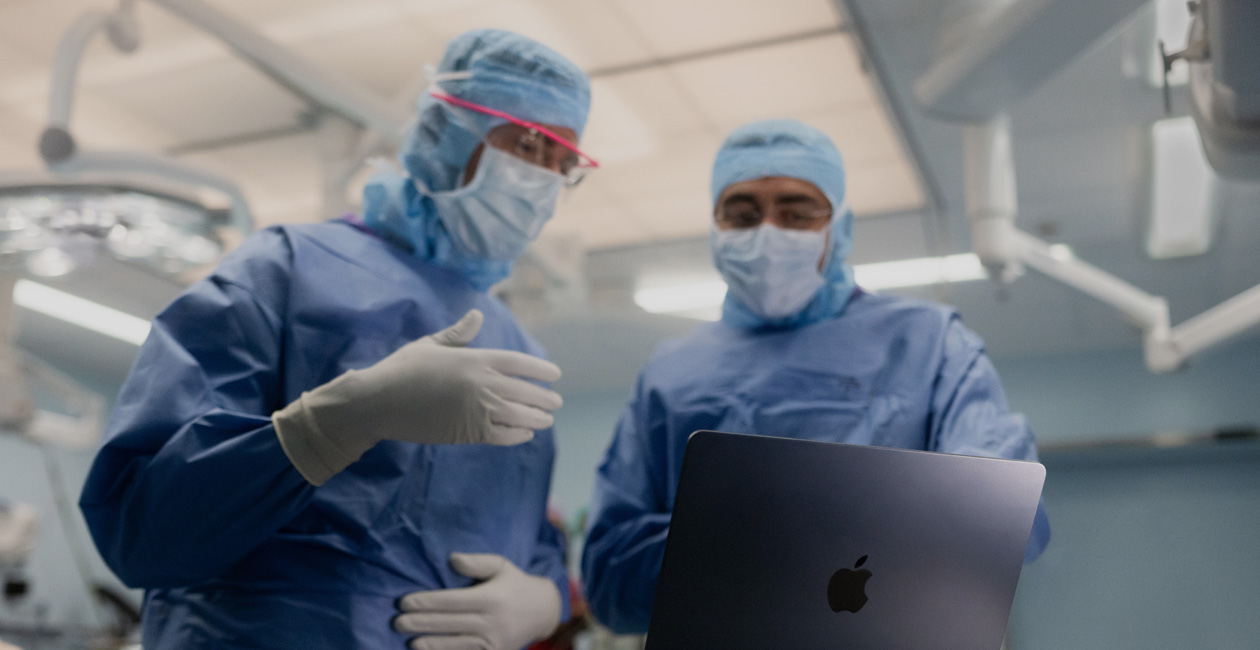 手術室でMacBook Proの画面を見ながら話し合う2人の外科医