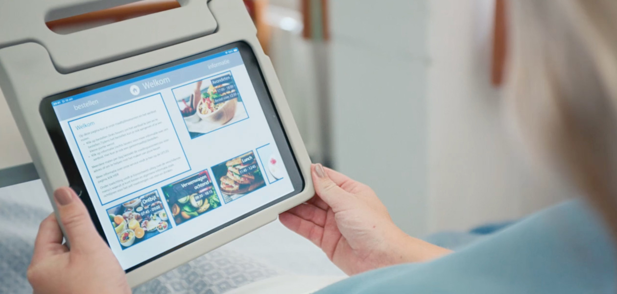 病院のベッドに座ってiPadの画面を見ている患者