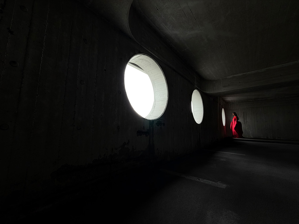 Una mujer con un largo vestido rojo de pie en medio de una habitación vacía mientras la fotografían. La distancia focal de la imagen se va alternando en la app Fotos para mostrar las capacidades del sistema de cámaras Pro: 13 mm