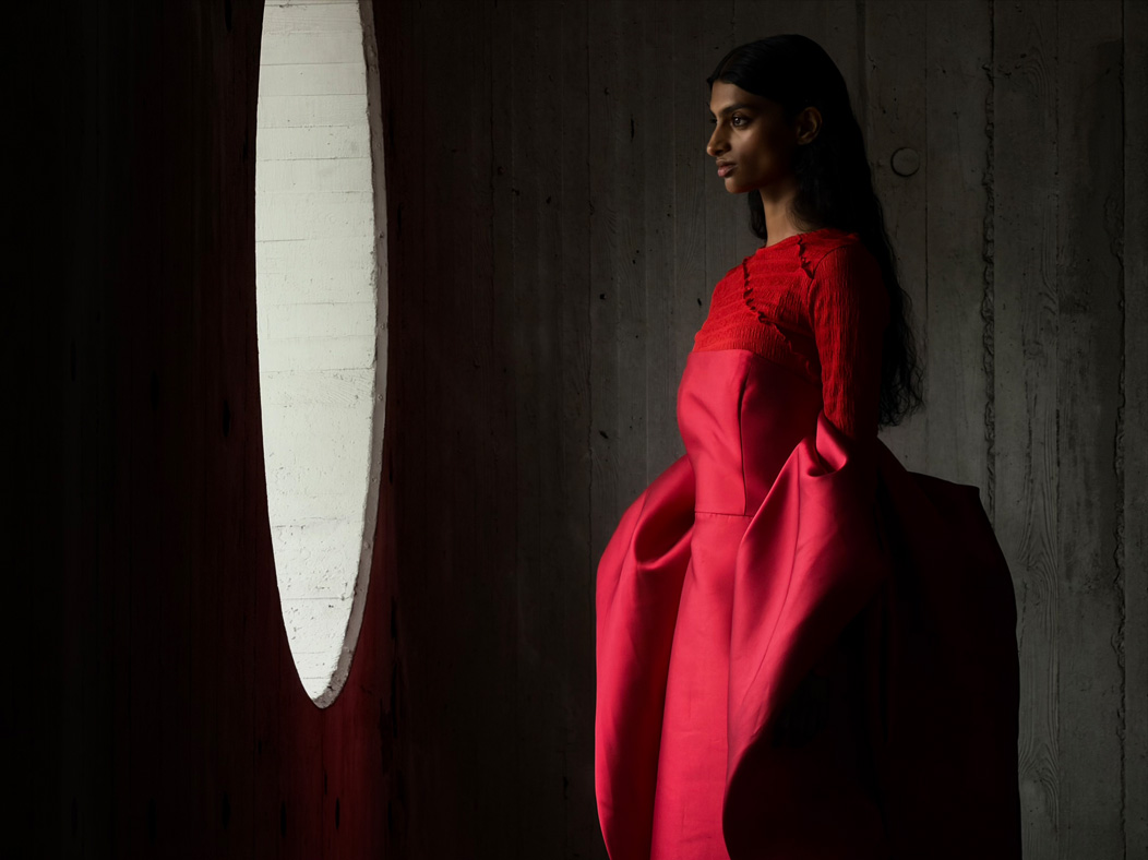 Una mujer con un largo vestido rojo de pie en medio de una habitación vacía mientras la fotografían. La app Fotos alterna entre varias distancias focales para mostrar las capacidades del sistema de cámaras Pro: 200 mm