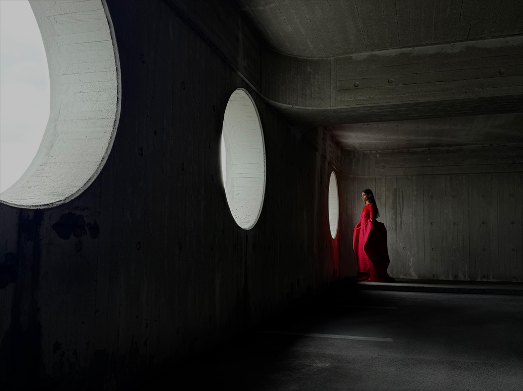 Una mujer con un largo vestido rojo de pie en medio de una habitación vacía mientras la fotografían. La distancia focal de la imagen se va alternando en la app Fotos para mostrar las capacidades del sistema de cámaras Pro: 35 mm