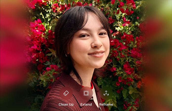 Photo of smiling person with brown hair, wearing a brown sweater, surrounded by red flowers, AI photo editing demo with Clean Up, Extend, Reframe options shown over photo