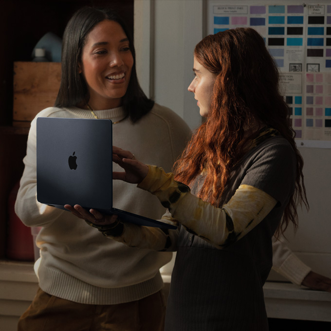 Una maestra y una estudiante conversan mientras sostienen una laptop MacBook